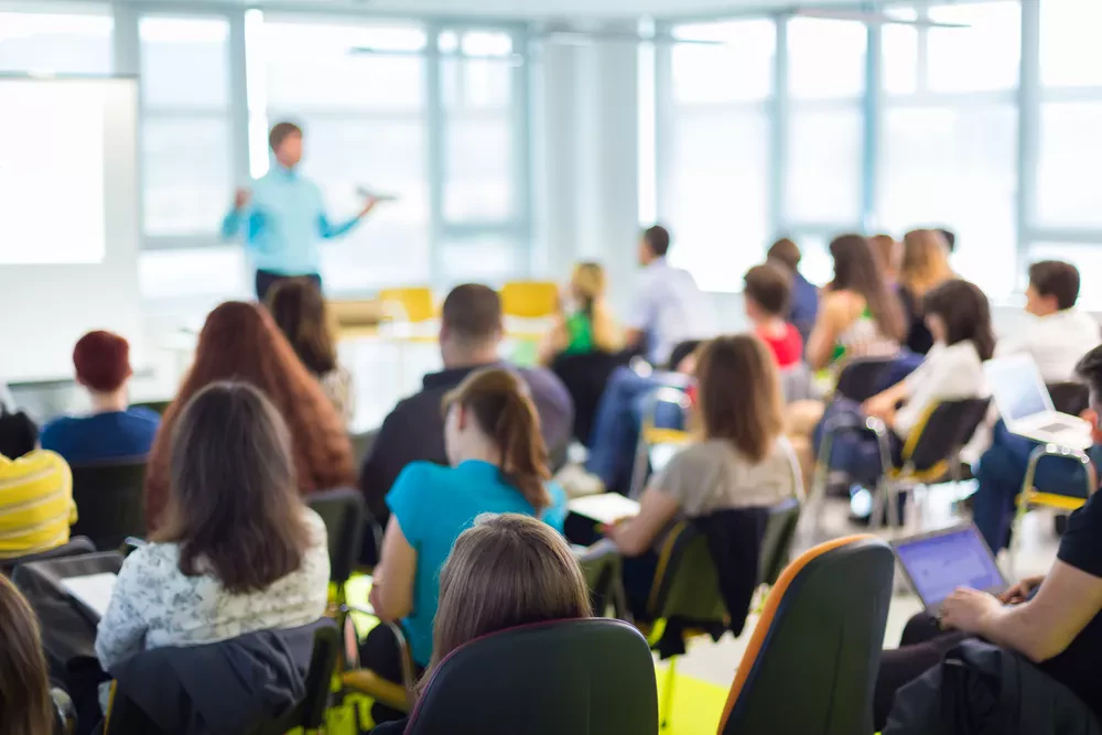 Classe de cours avec des élèves assis en premier plan qui écoutent un enseignants debout